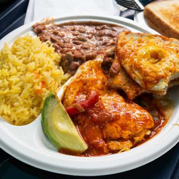 Plate of Mexican-style enchiladas with melted cheese, yellow rice, refried beans, avocado, salsa, and toasted bread.